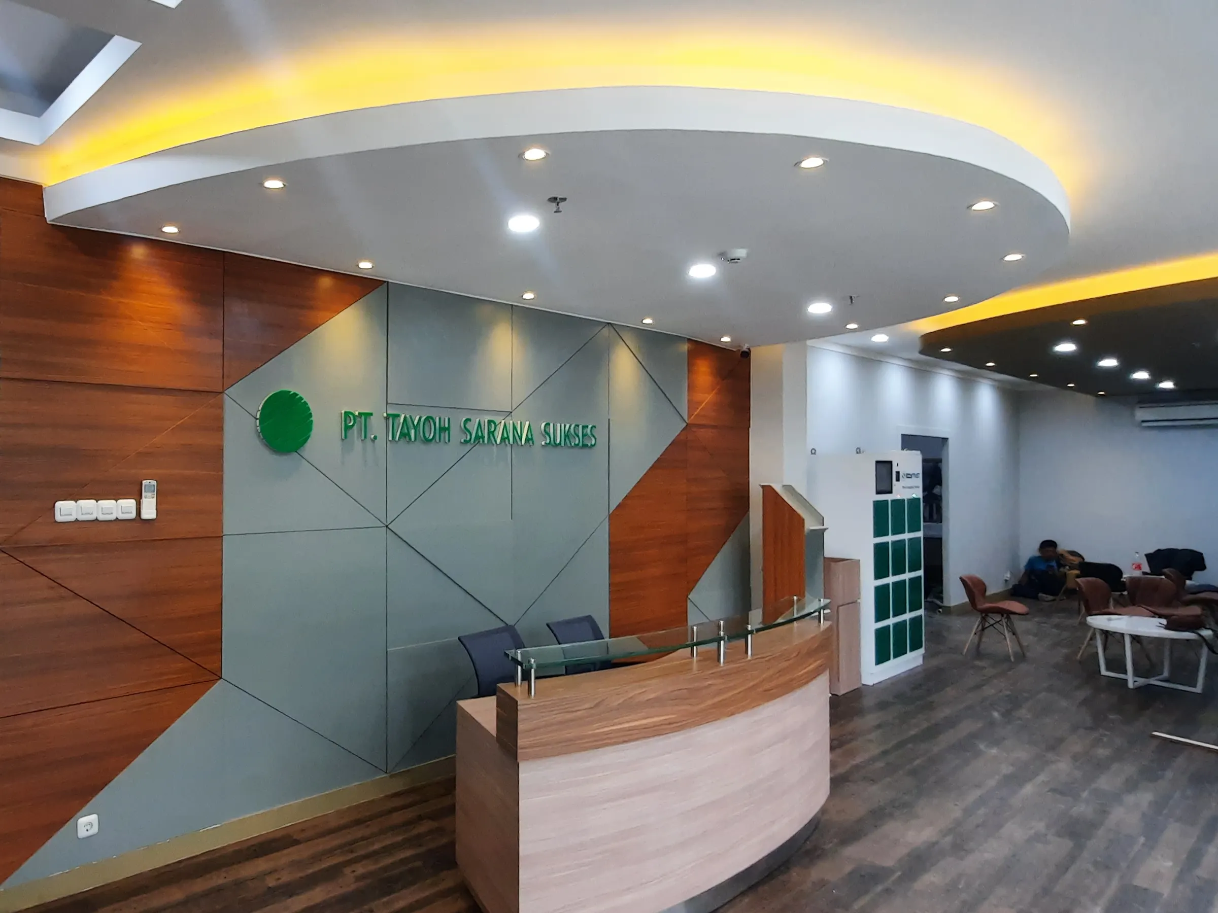 proyek-lobi-kantor-pt-tayoh-sarana-sukses Desain interior ruang tunggu kantor menampilkan kombinasi dinding panel kayu, dekorasi abu-abu geometris, dan lampu plafon hangat